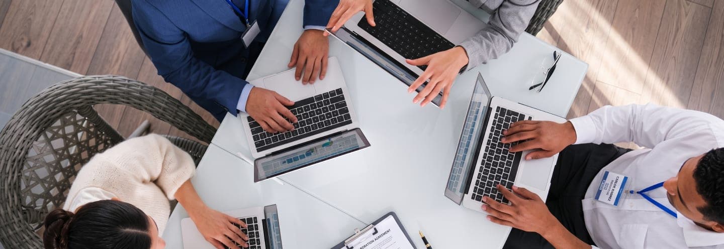 Equipo comercial trabajando en conjunto alrededor de una mesa con laptops