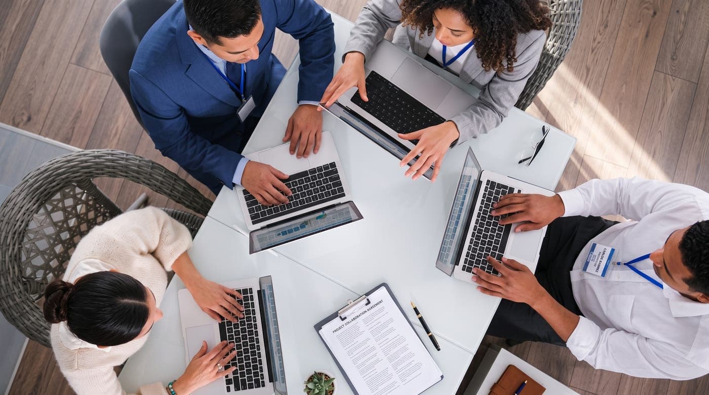 Equipo comercial trabajando con laptops alrededor de una mesa
